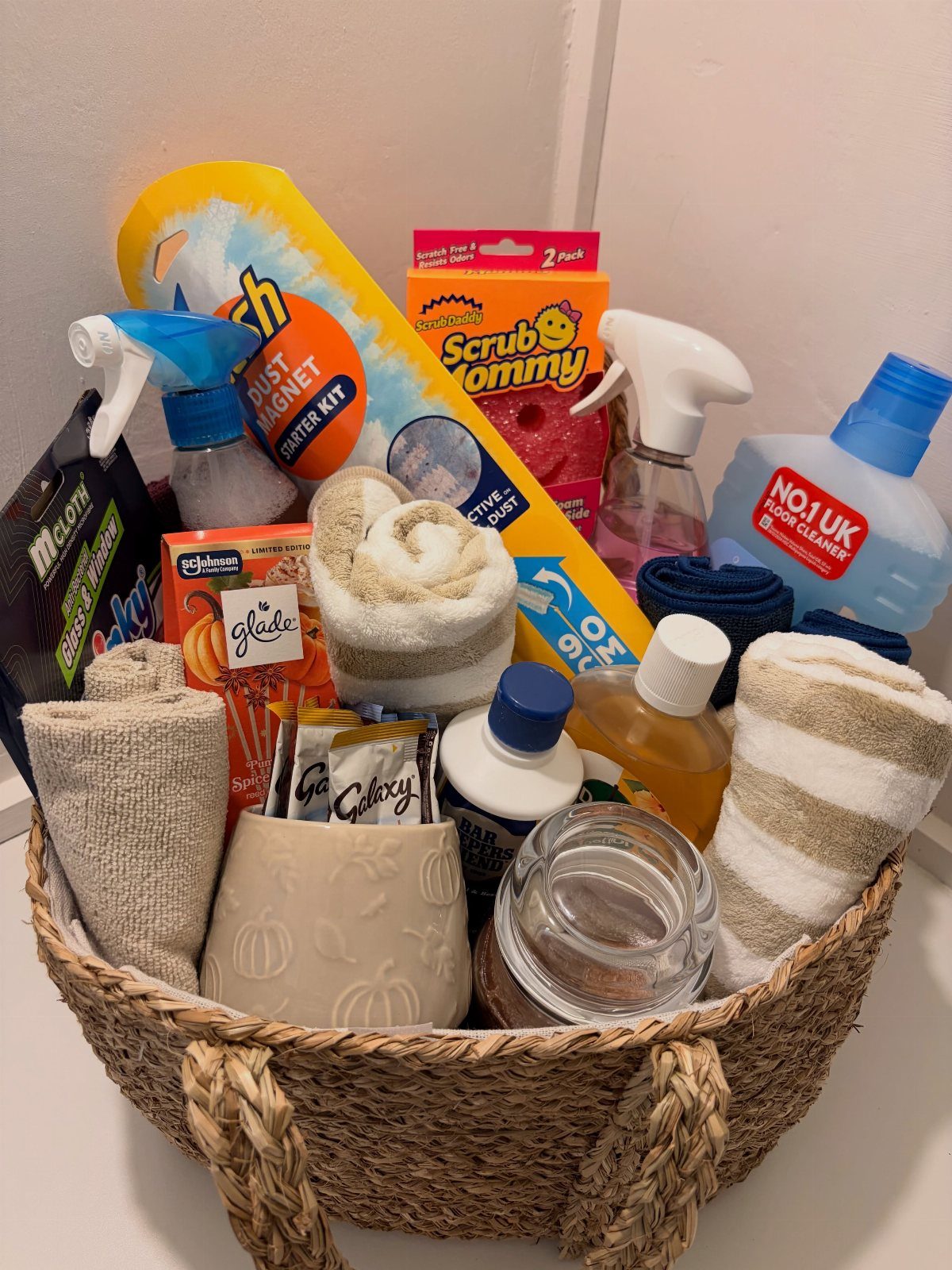 Woven wicker basket filled with various cleaning supplies, sponges, and microfiber cloths.