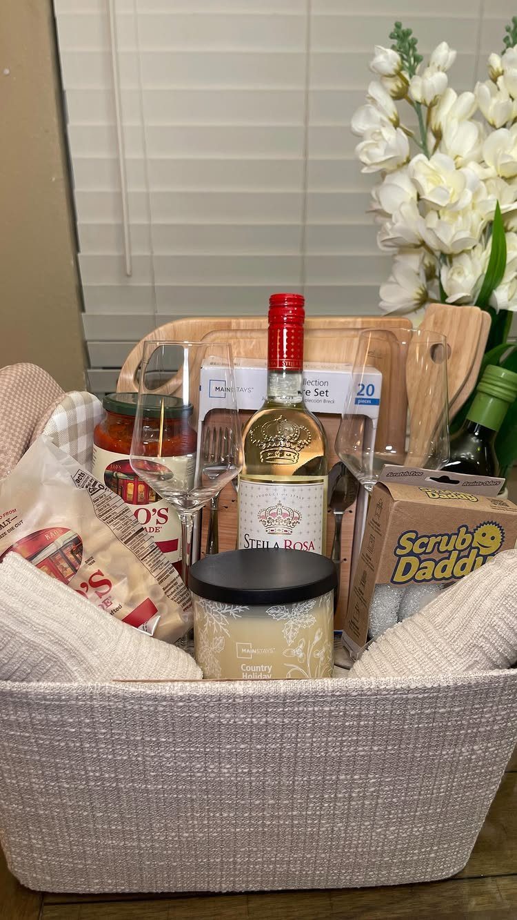 Woven gift basket with wine, pasta sauce, candle, and cleaning supplies for housewarming.