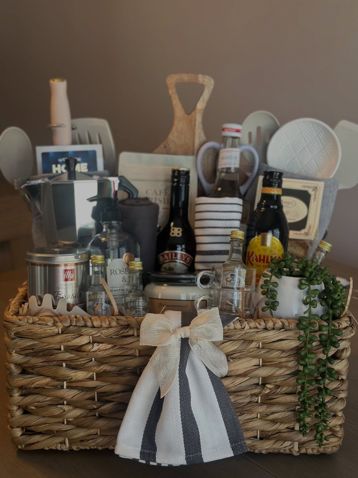Woven gift basket filled with a Moka pot, kitchen utensils, and gourmet bottles.
