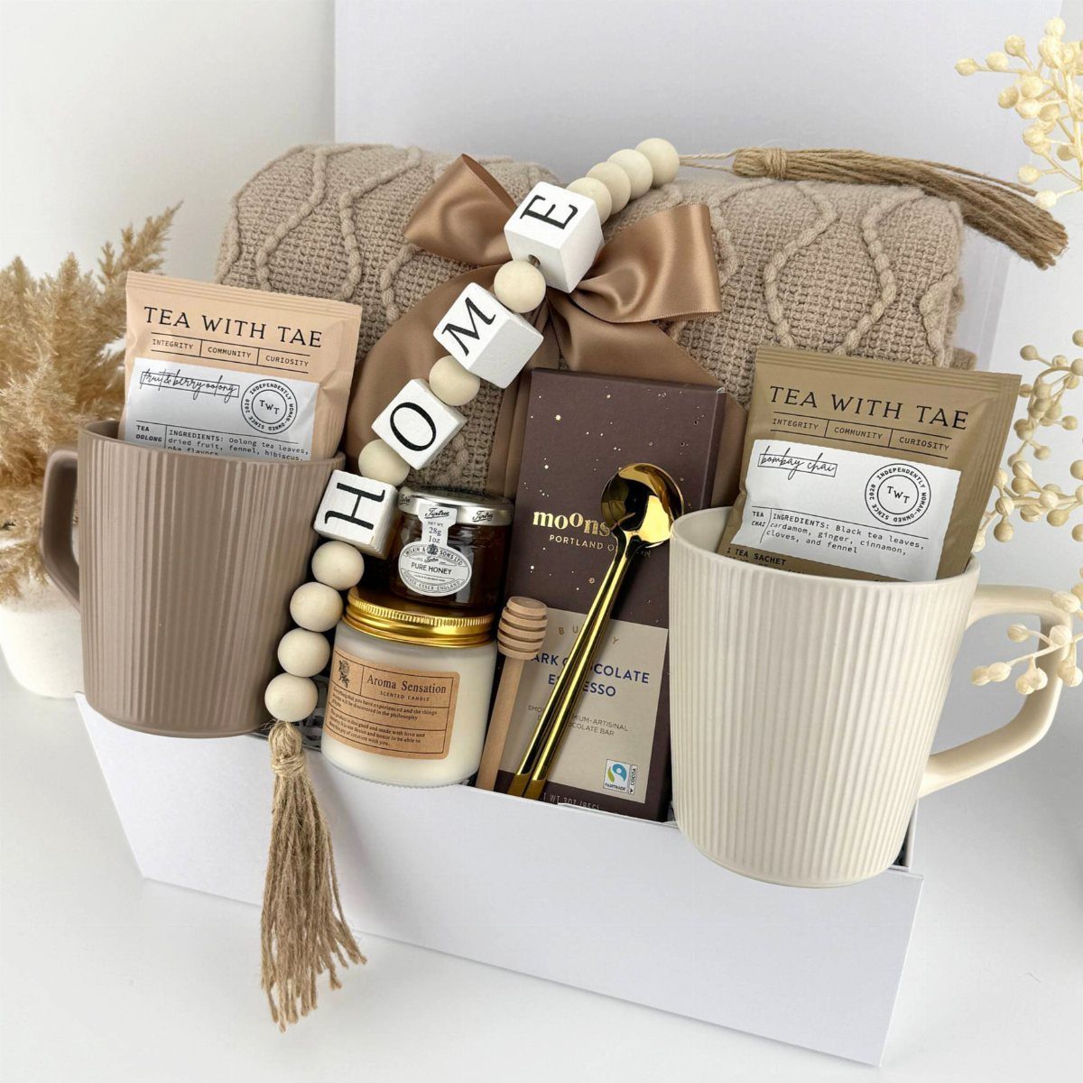 Gift box with tea, honey, chocolate, and a beige throw blanket for housewarming.
