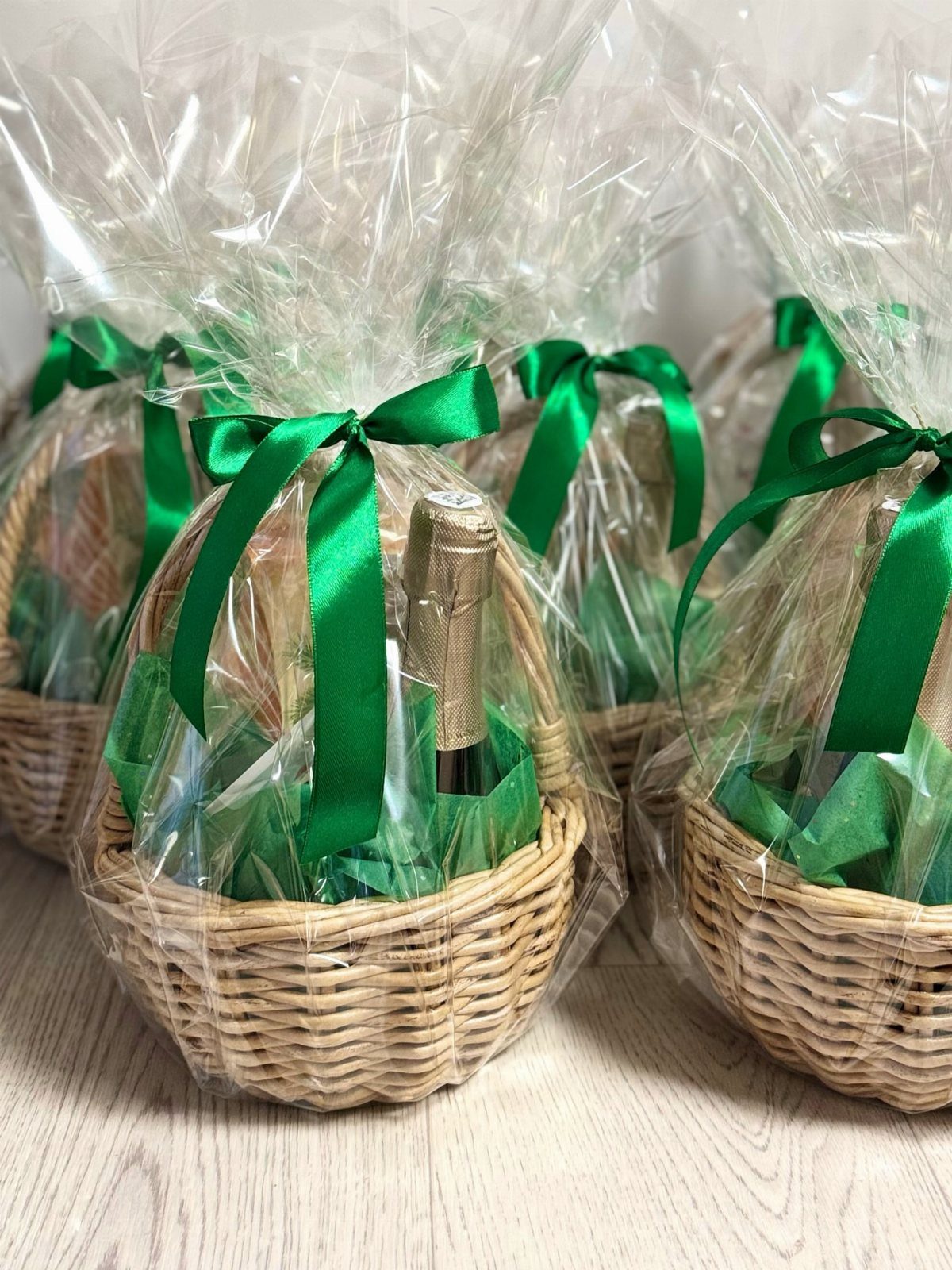 Wicker gift baskets wrapped in cellophane with green bows and champagne bottles.