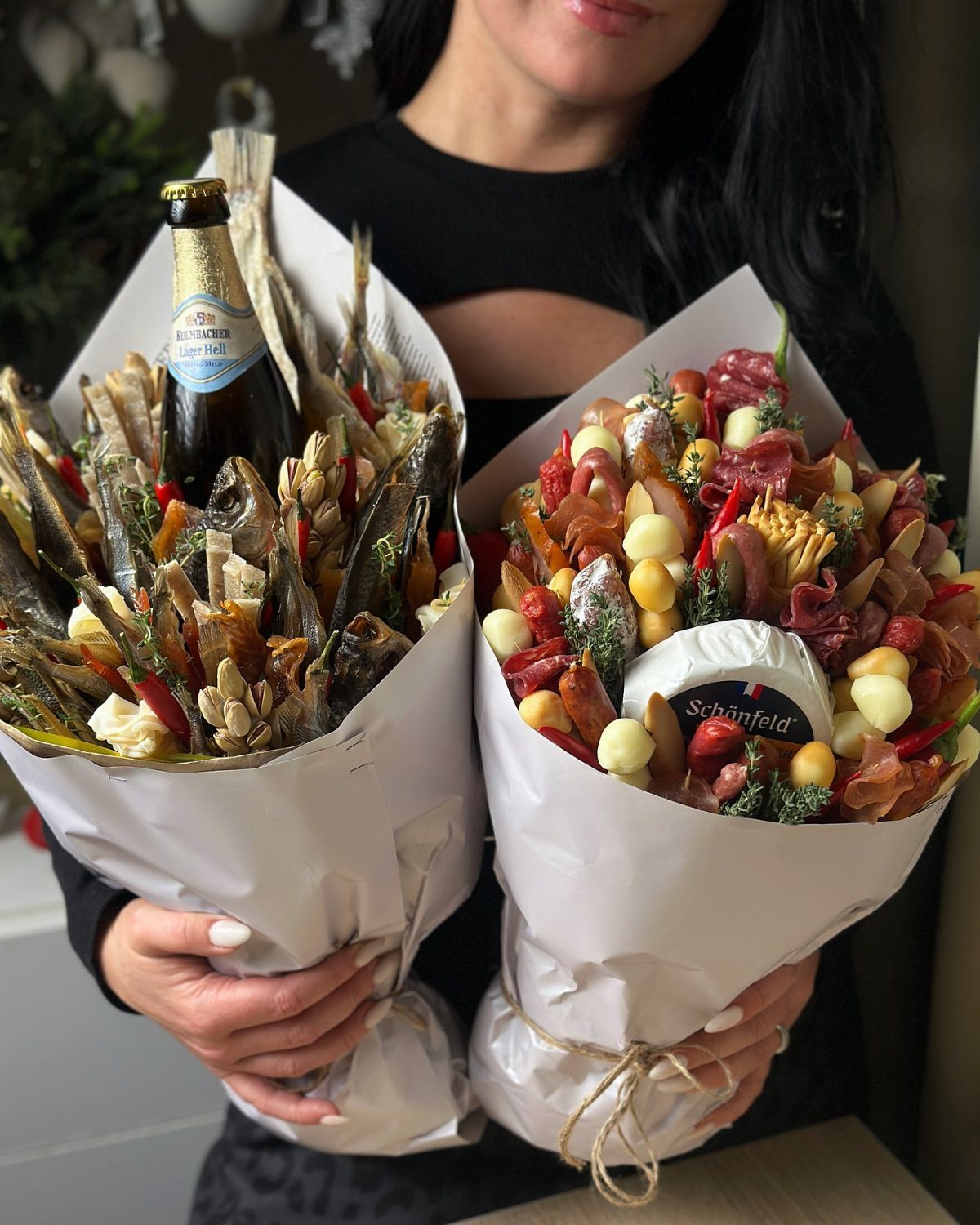 Two edible bouquets filled with meats, fish, and beer held by a person.