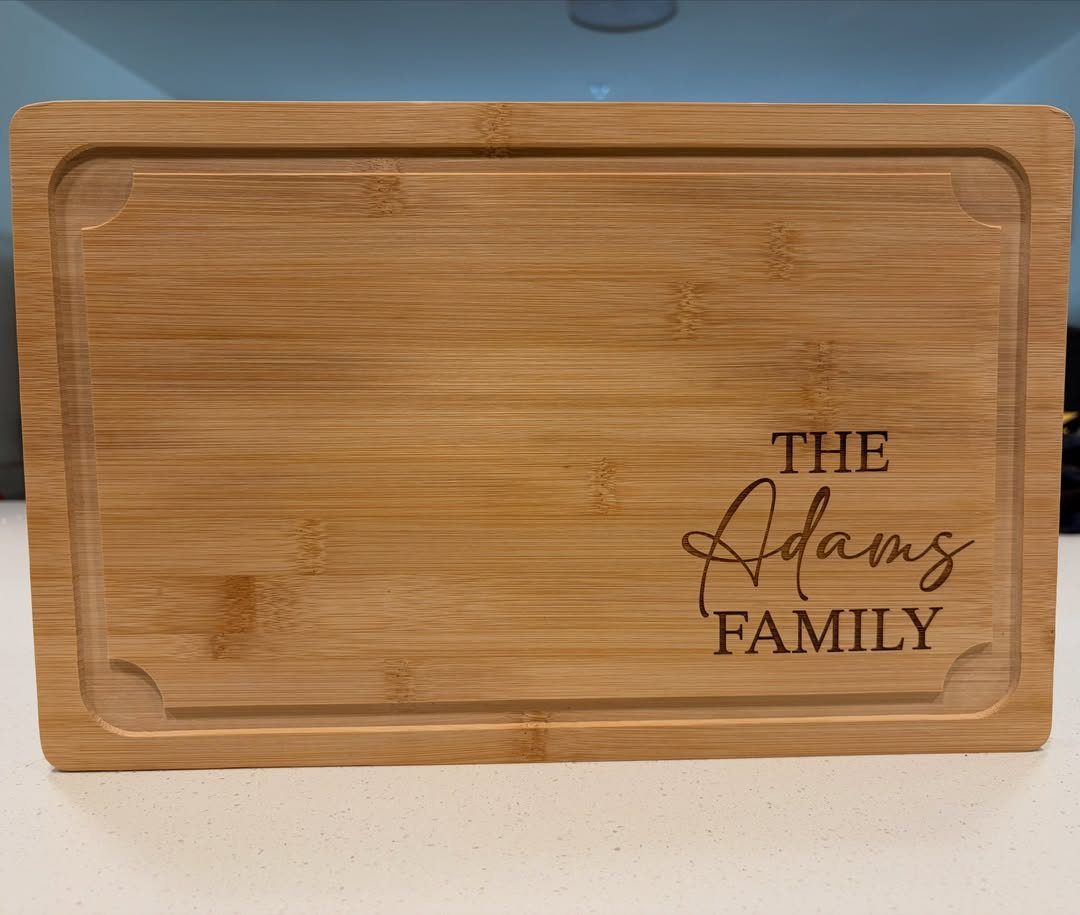 Bamboo cutting board engraved with The Adams Family text on a white surface
