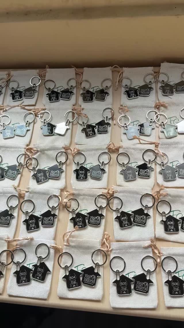 House-shaped metal keychains with engravings resting on white fabric pouches in a tray.