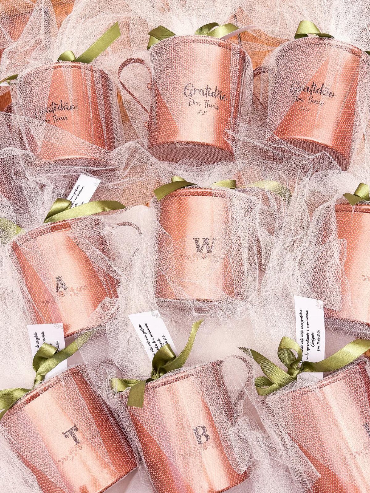 Copper mugs wrapped in white tulle with green ribbons and engraved letters.