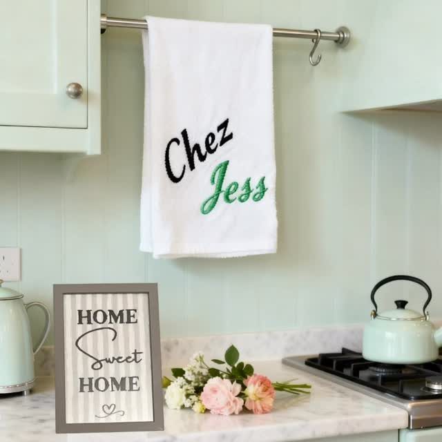 White embroidered kitchen towel hanging in a kitchen with a home decor sign.