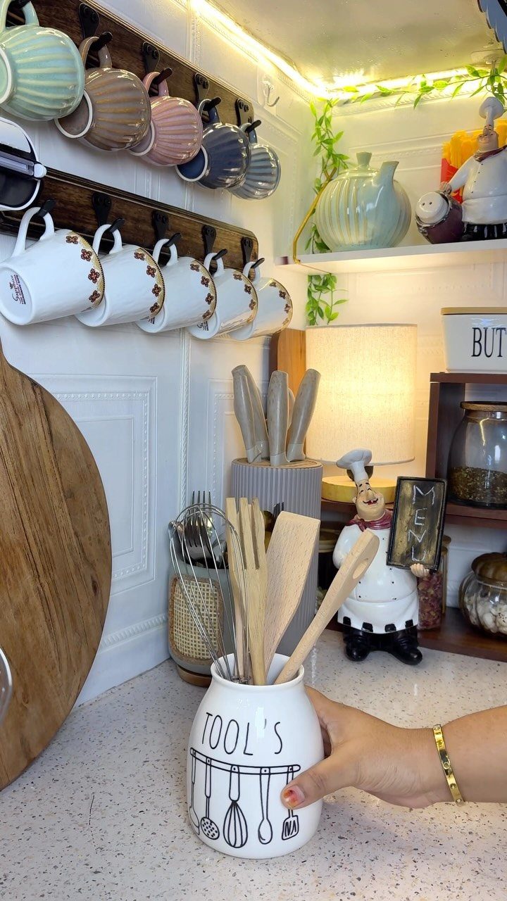 White ceramic utensil holder with wooden spoons in a decorated kitchen setting