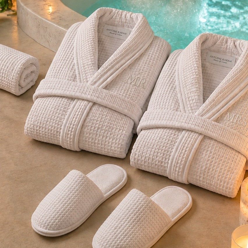 Two white embroidered terry bathrobes and matching slippers by a swimming pool.