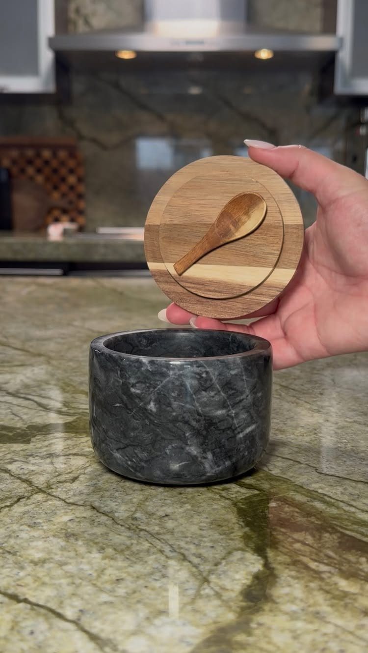 Small dark marble container with a wooden lid and spoon on a countertop.