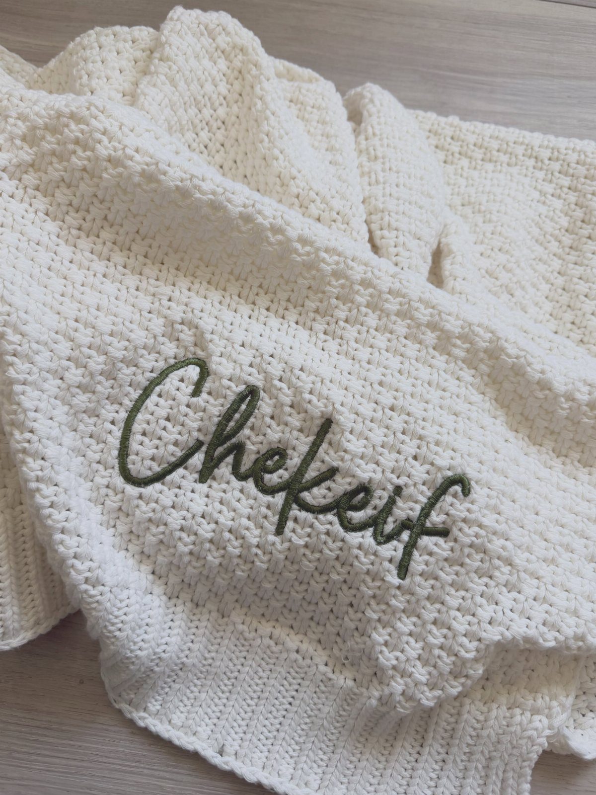 Cream knitted blanket with the name Chekeif embroidered in green cursive script.