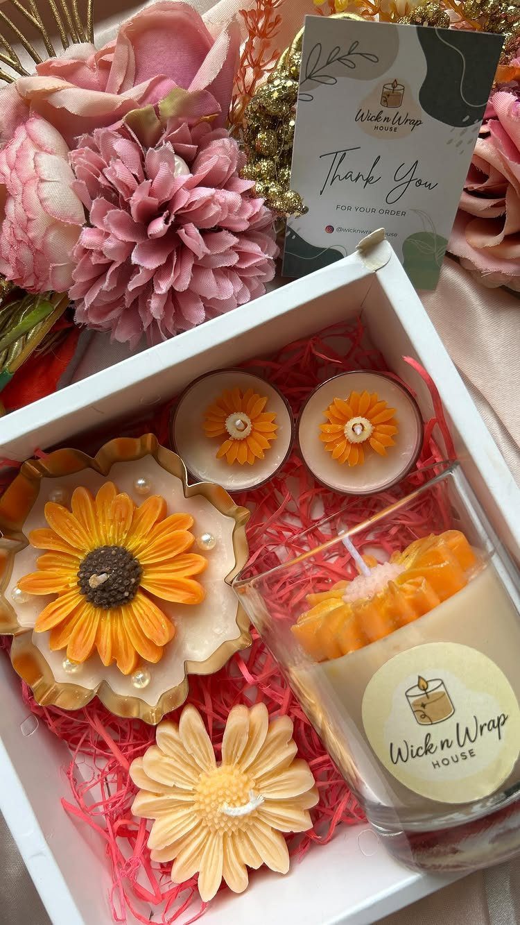Assorted flower-shaped candles and a jar candle in a white gift box.