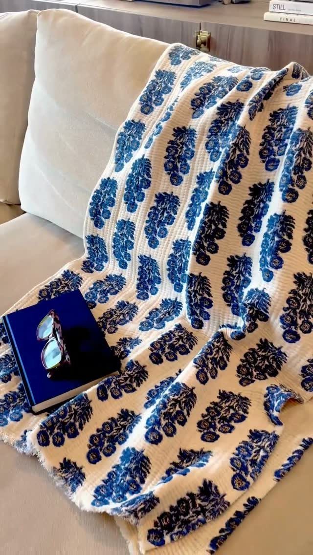 Blue and white floral throw blanket draped over a white sofa with a book.