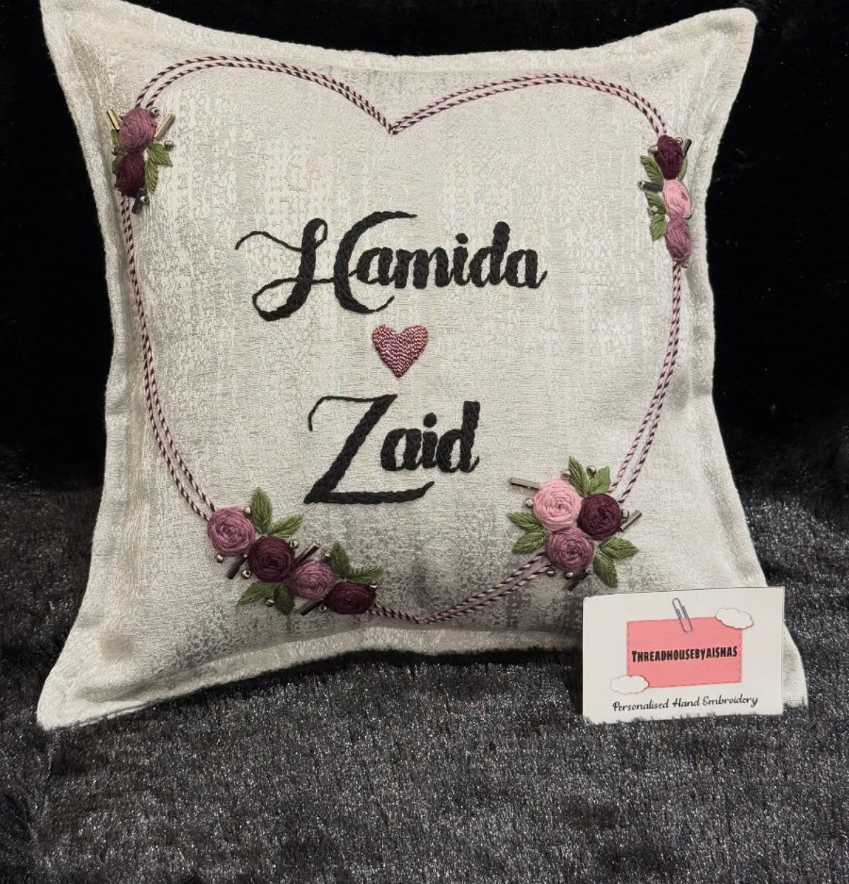Customized off-white pillow with embroidered names Hamida and Zaid inside a floral heart.