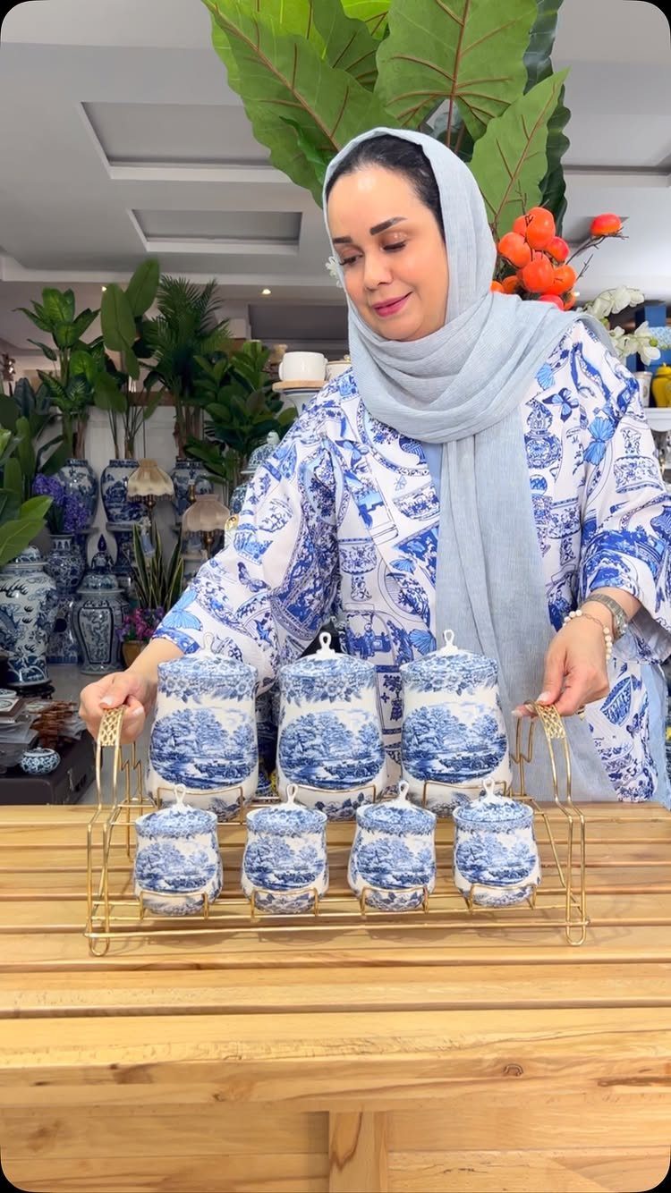Woman presenting blue and white ceramic canisters on a gold metal rack.