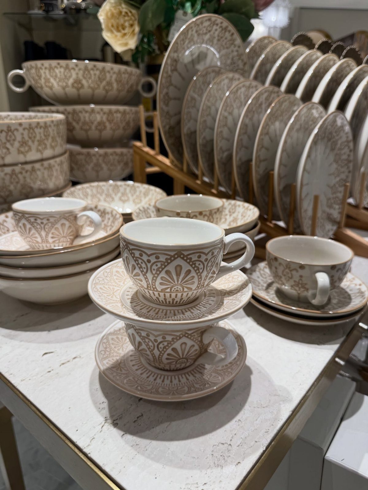 Beige and brown patterned dinnerware set with plates, bowls, and teacups on marble.