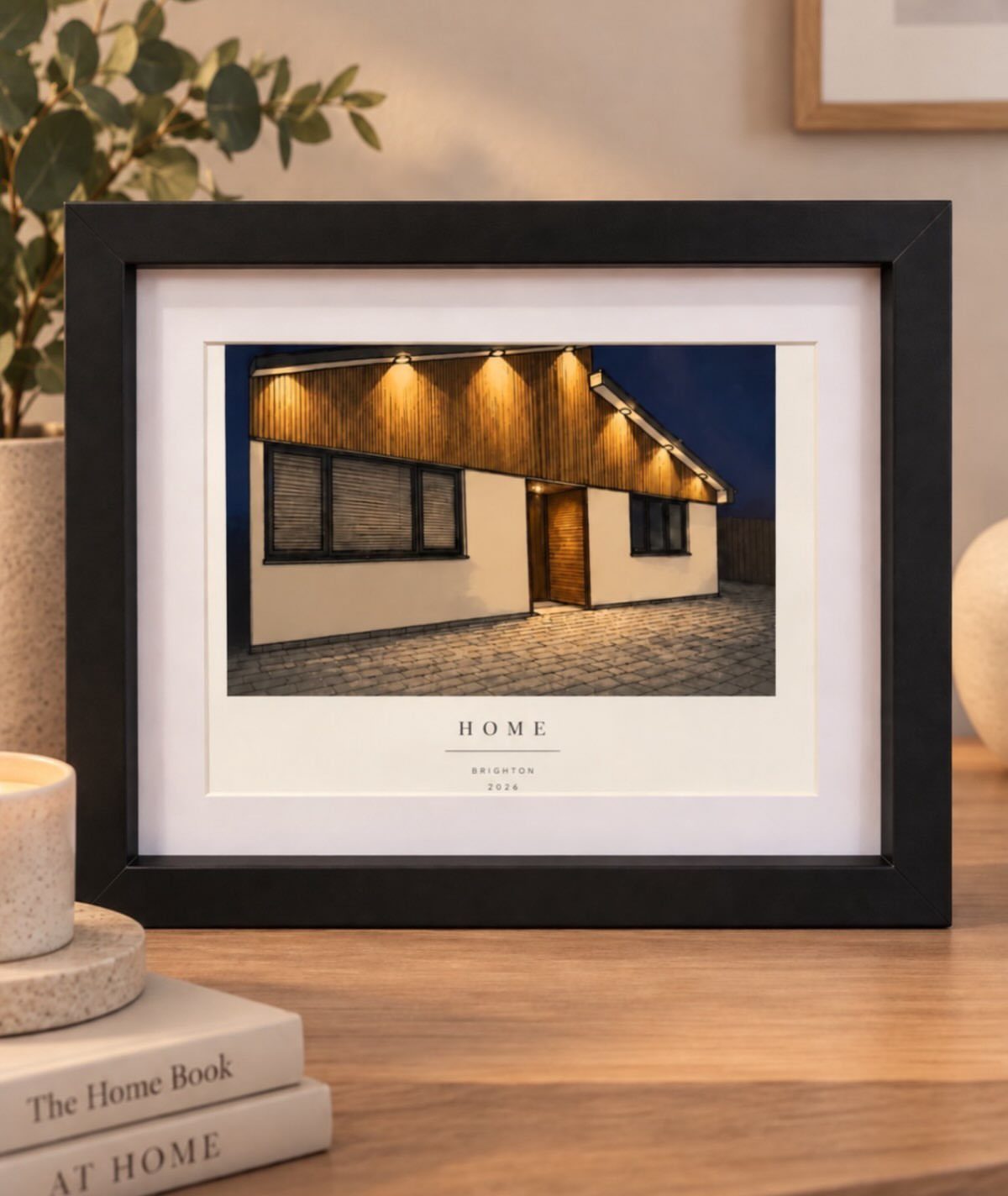 Black framed print of a modern house at night on a wooden table