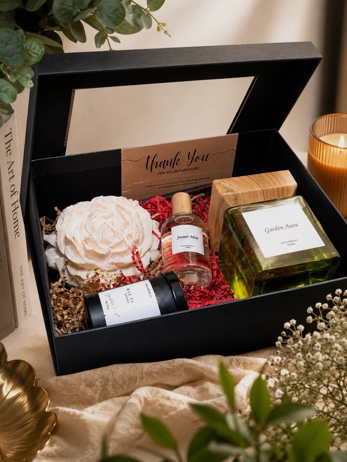 Gift box with a black candle, essential oils, and a white decorative flower.