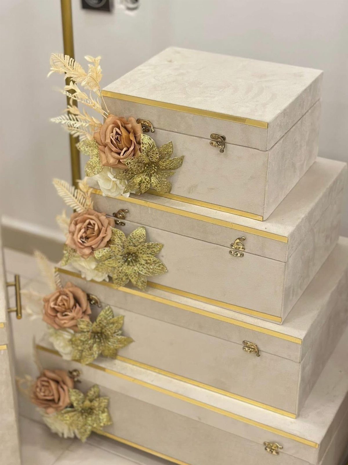 Stacked cream storage boxes with gold trim and artificial floral decorations on the side.