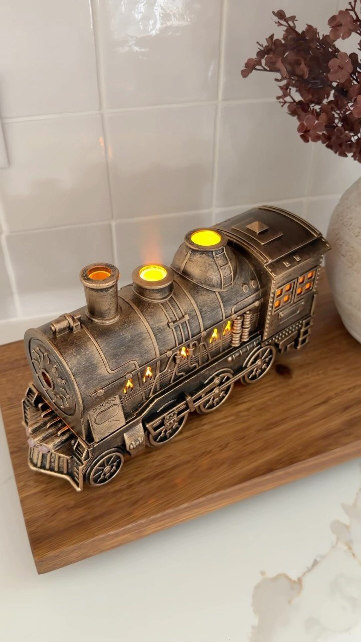 Bronze steam locomotive wax warmer glowing on a wooden shelf against white tiles.