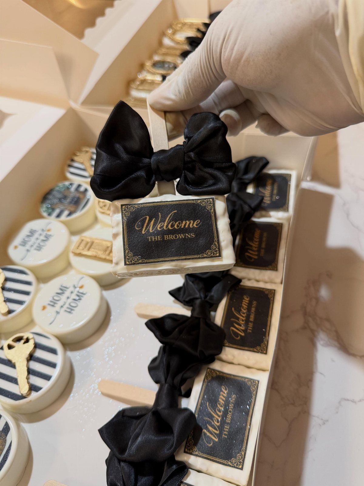 Decorated sugar cookies with black bows and welcome messages in a white box