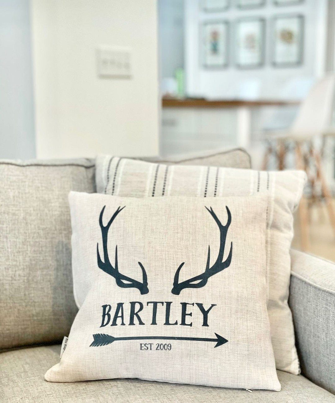 Personalized beige throw pillow with antler design and name on a grey sofa