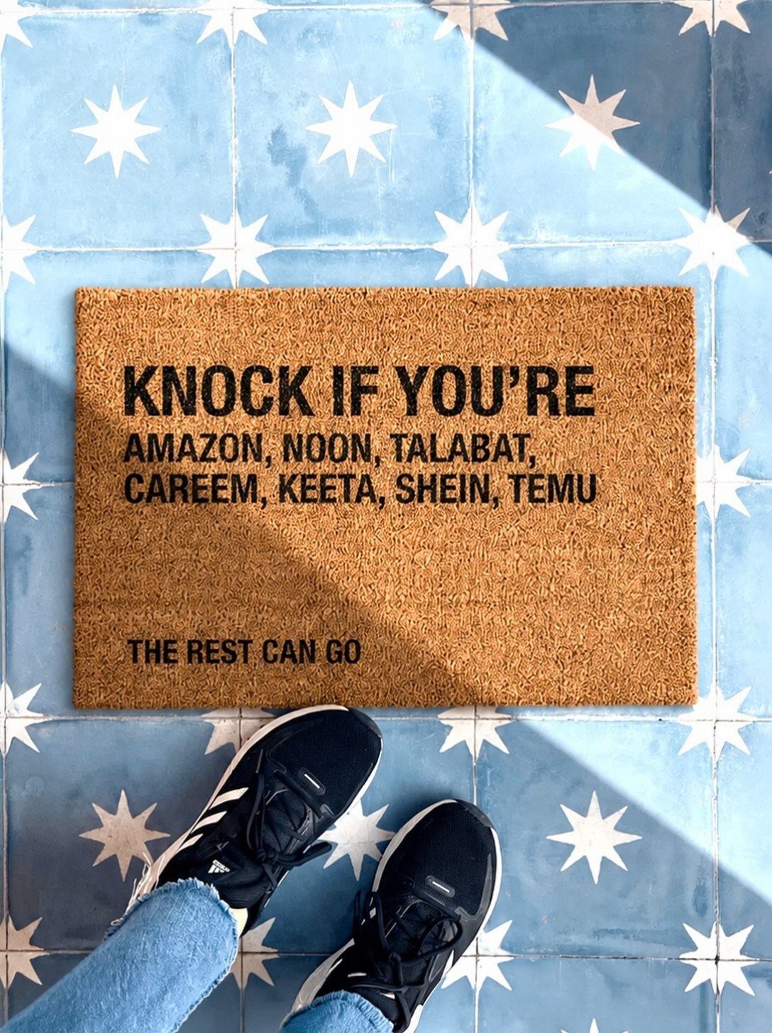 Brown coir doormat with delivery service text on blue star-patterned tiles.