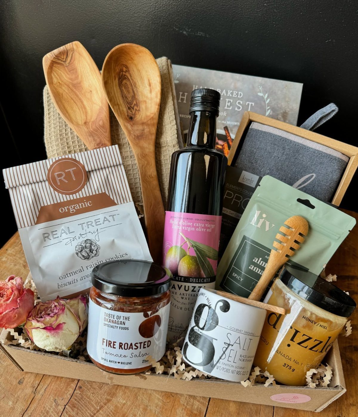 Gourmet gift basket containing olive oil, salsa, honey, cookies, and wooden spoons.