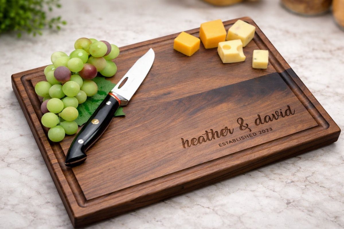 Engraved wooden cutting board with grapes, cheese cubes, and a knife on marble.
