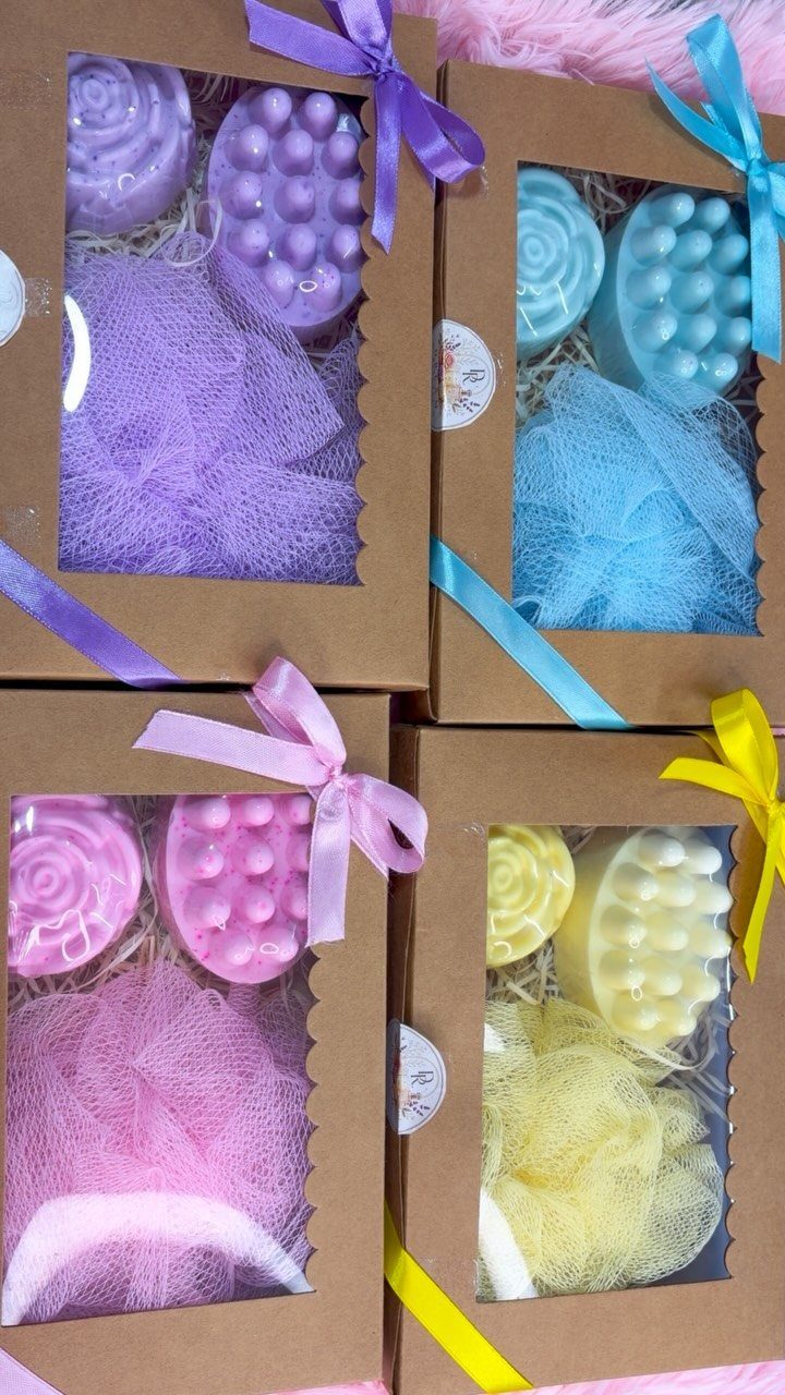 Four colorful bath gift sets in brown boxes with matching ribbons and sponges.