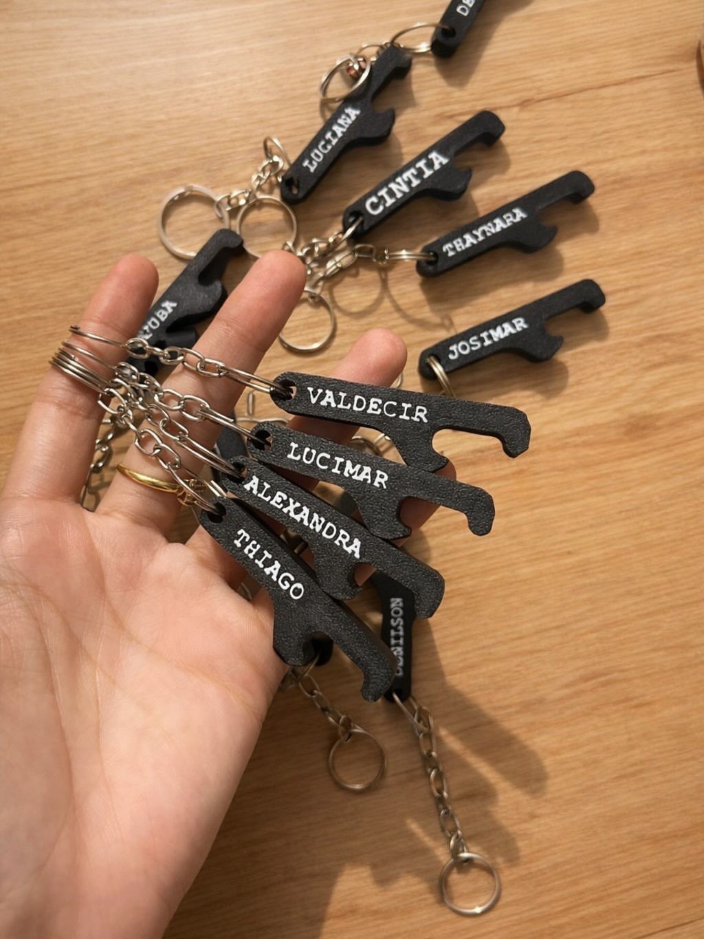 Black metal bottle opener keychains with personalized names held in a hand.