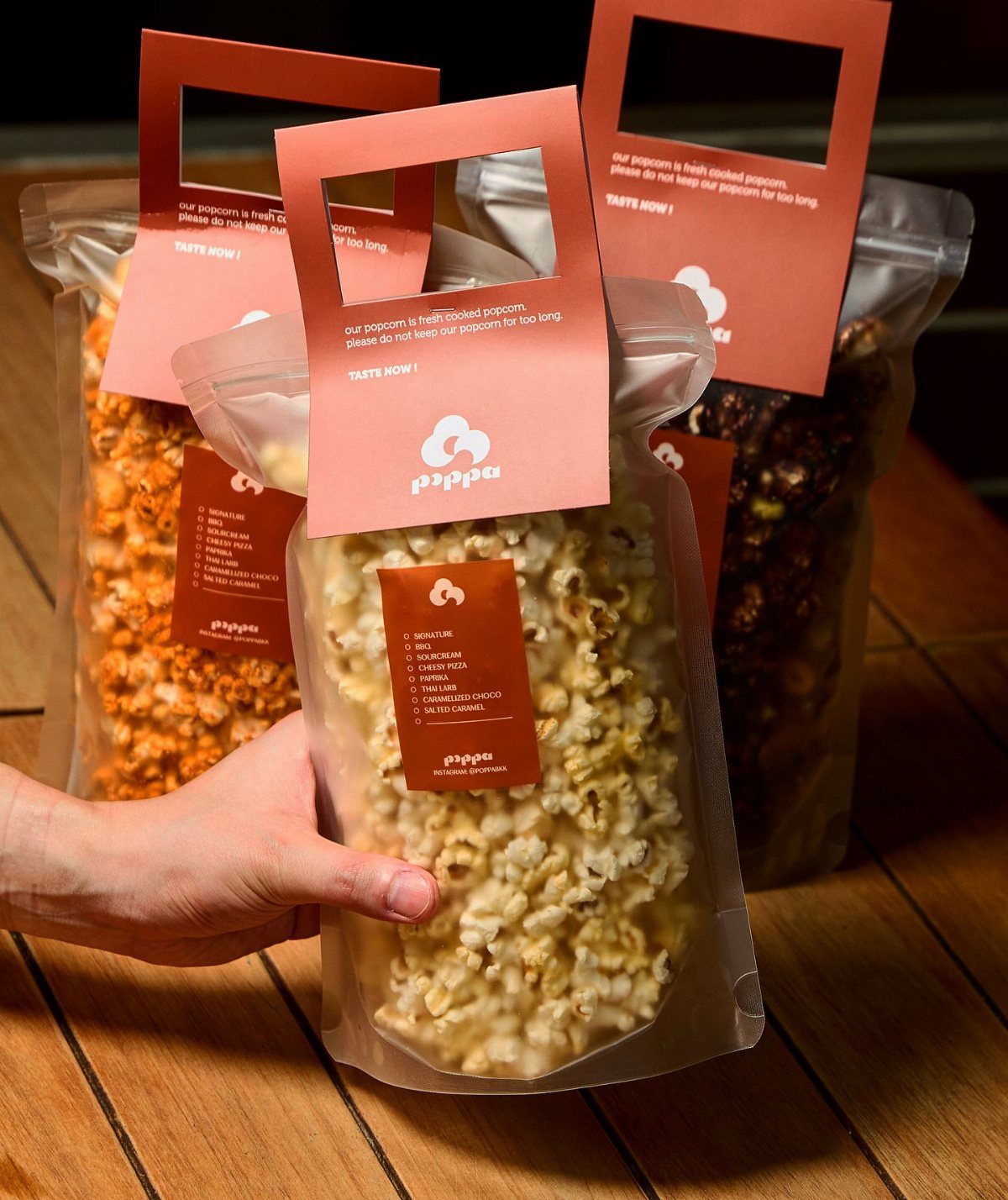 Clear plastic bags of gourmet popcorn with red labels on a wooden table.