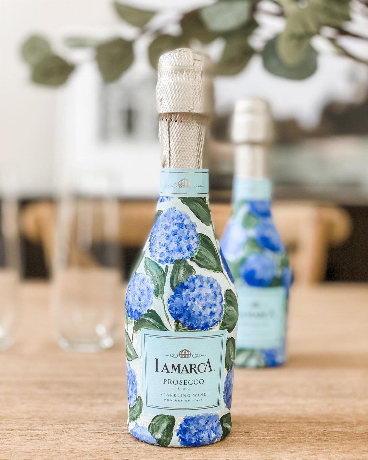 Mini Prosecco bottles wrapped in blue floral paper on a wooden table.