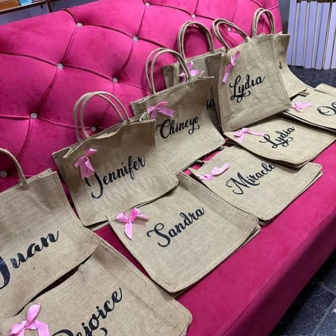 Burlap tote bags with personalized names and pink ribbons on a pink sofa.