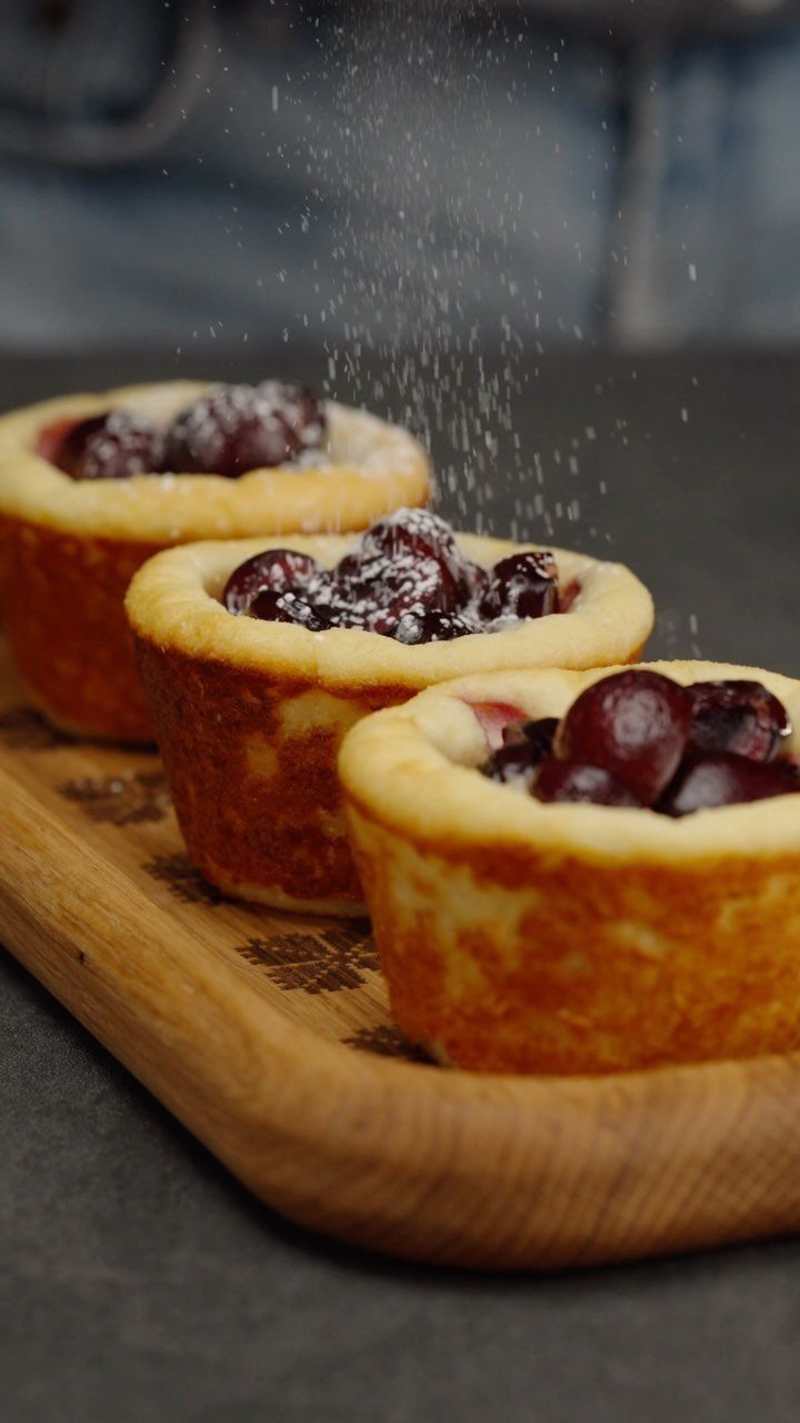 Mini cherry cheesecakes on a wooden board with powdered sugar falling on top