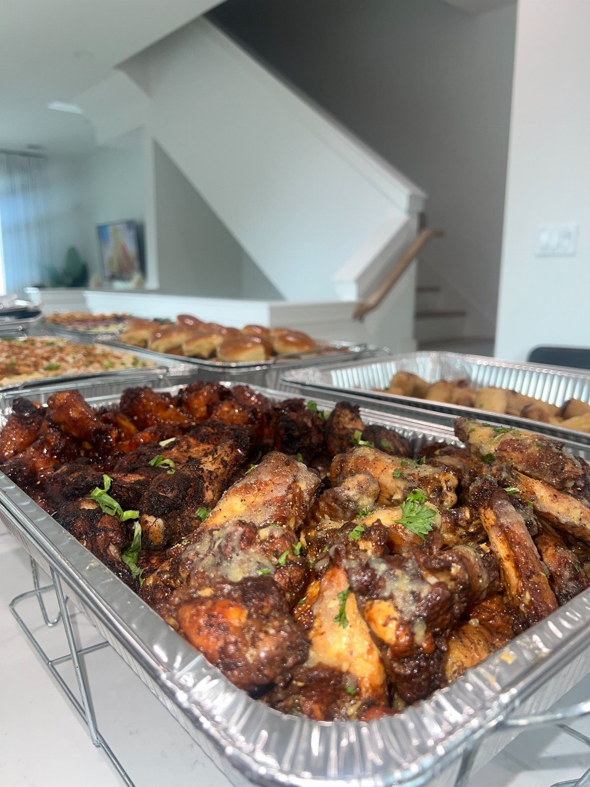 Glazed chicken wings in an aluminum tray with sliders and pizza in background