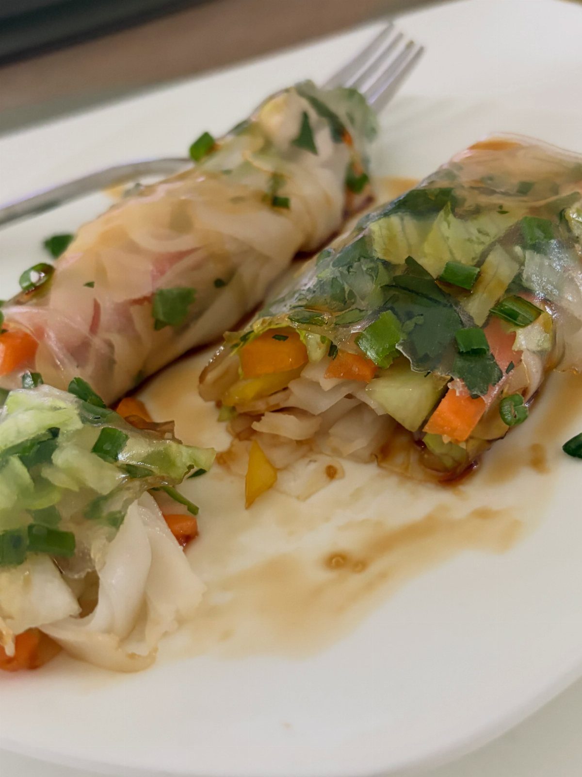 Fresh spring rolls with vegetables and herbs on a white plate with sauce.
