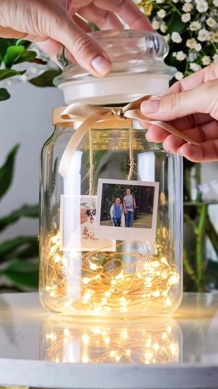 Glass jar with fairy lights, a candle, and photos tied with a ribbon.