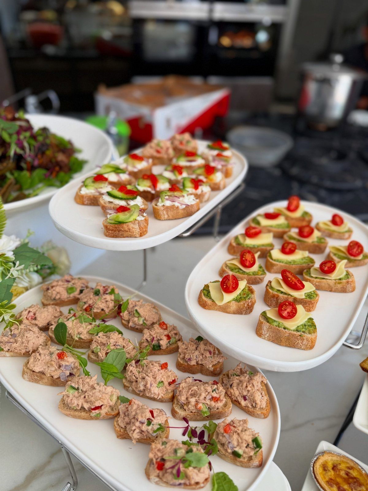 Assorted appetizers on white platters including avocado bruschetta and tuna salad toasts.