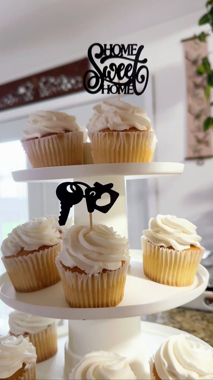 Vanilla cupcakes with white frosting and house-themed black cake toppers on a stand.