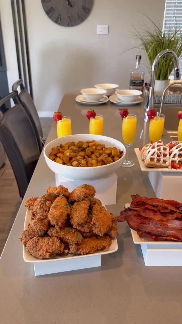 Brunch spread with fried chicken, bacon, potatoes, and orange juice on a counter.