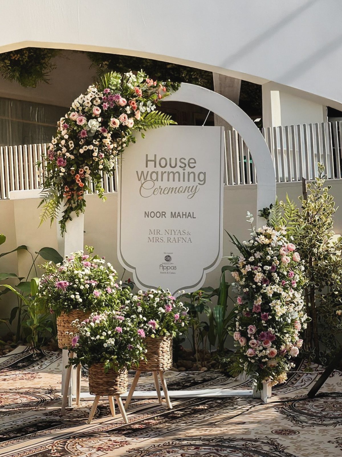 White housewarming ceremony arch decorated with pink and white flowers and baskets.