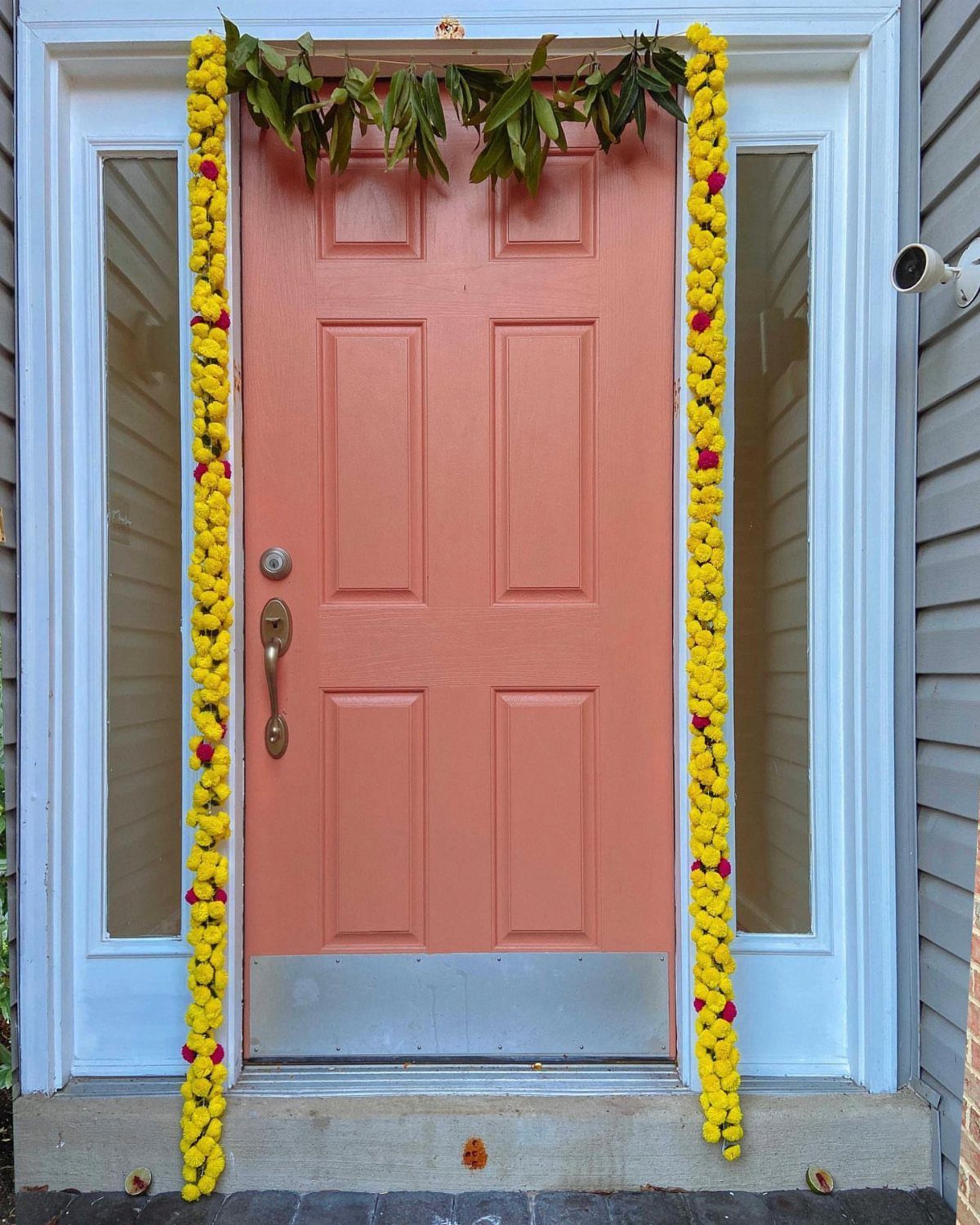 Peach front door decorated with yellow flower garlands and green leaf greenery.
