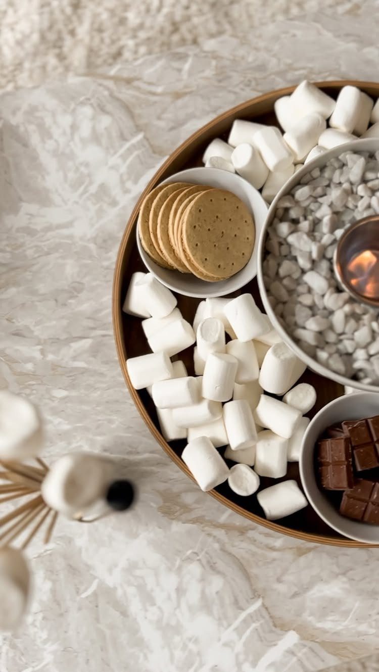 S'mores bar tray with marshmallows, graham crackers, chocolate, and a small tabletop fire pit.