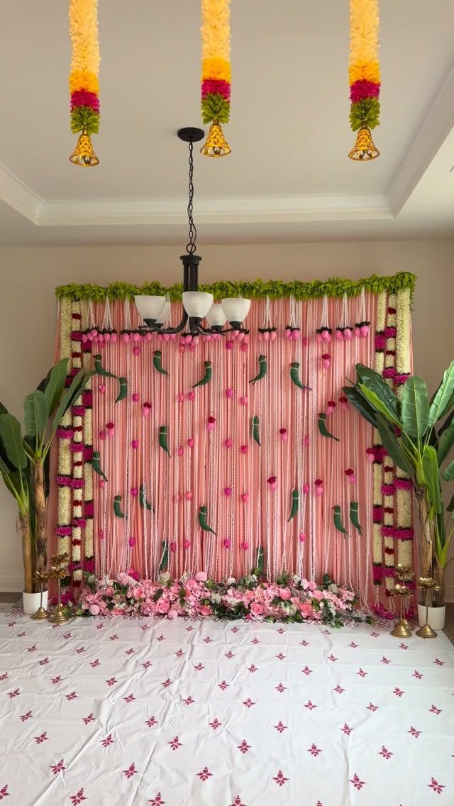 Decorative party backdrop with pink streamers, floral garlands, and green plants indoors.