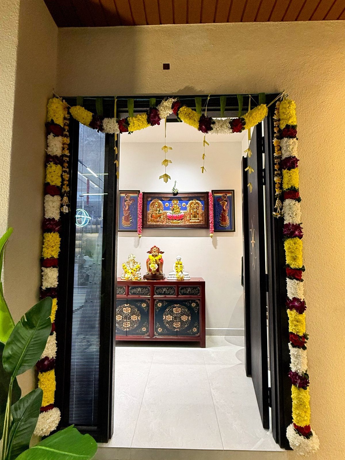 Flower decorated doorway leading to a room with religious art and a cabinet.
