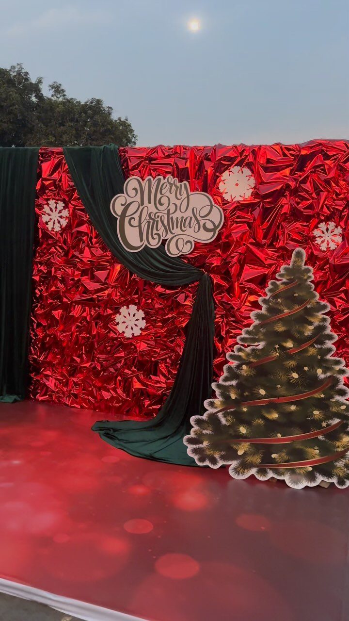 Christmas party backdrop with red foil wall, green drape, and tree cutout.