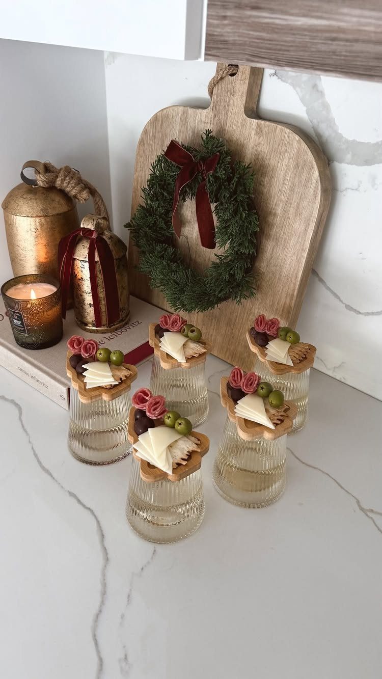 Small glasses of drinks topped with cheese and fruit appetizers near a wreath.