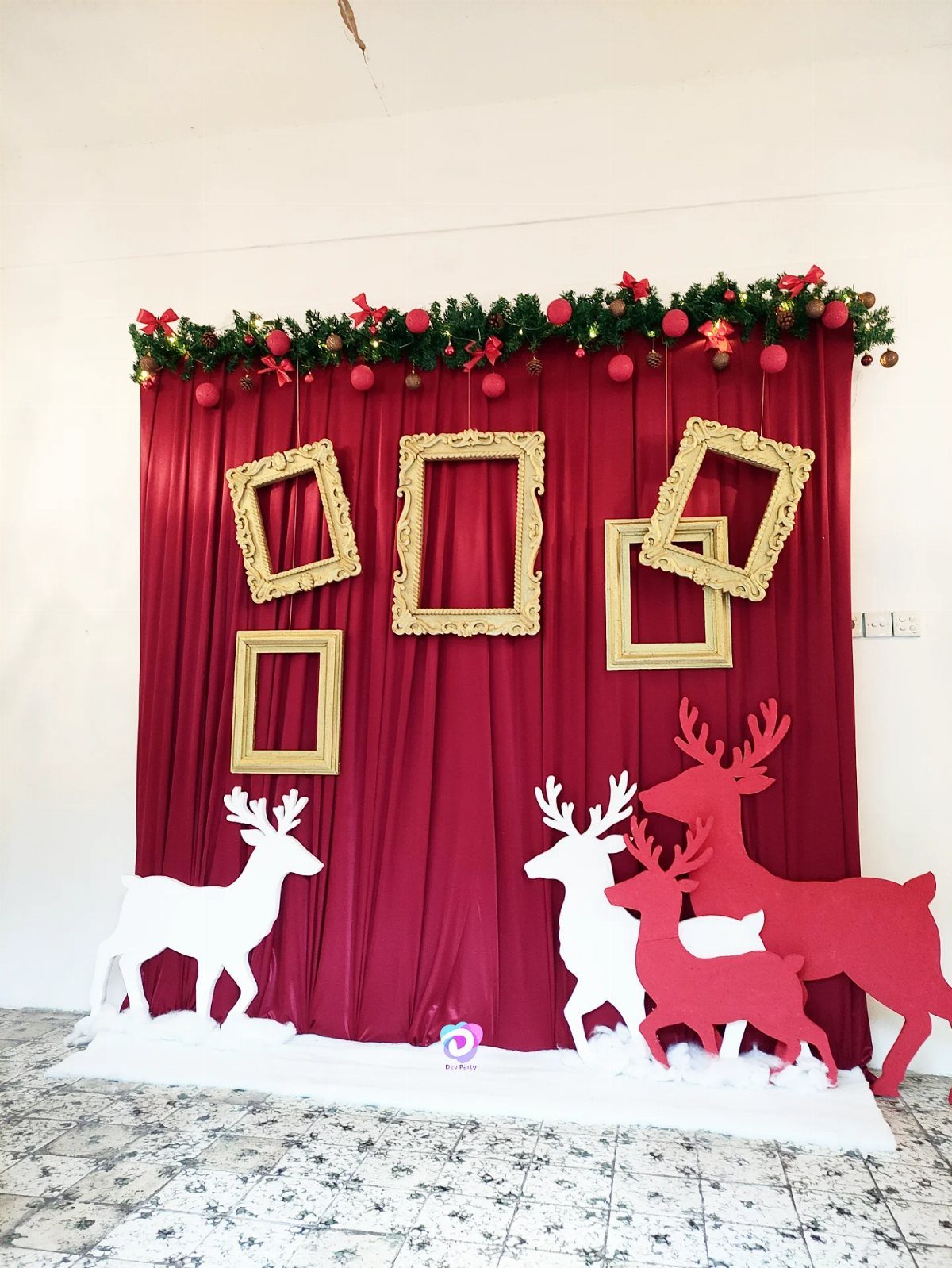 Festive photo booth with red curtain, gold frames, and reindeer cutouts.
