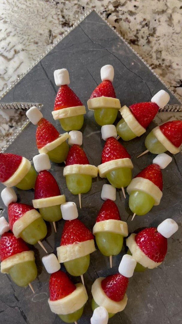 Fruit skewers shaped like Santa hats on a grey stone platter.