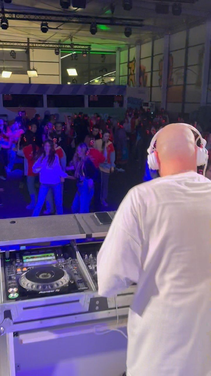 DJ with white headphones mixing music for a dancing crowd in a club
